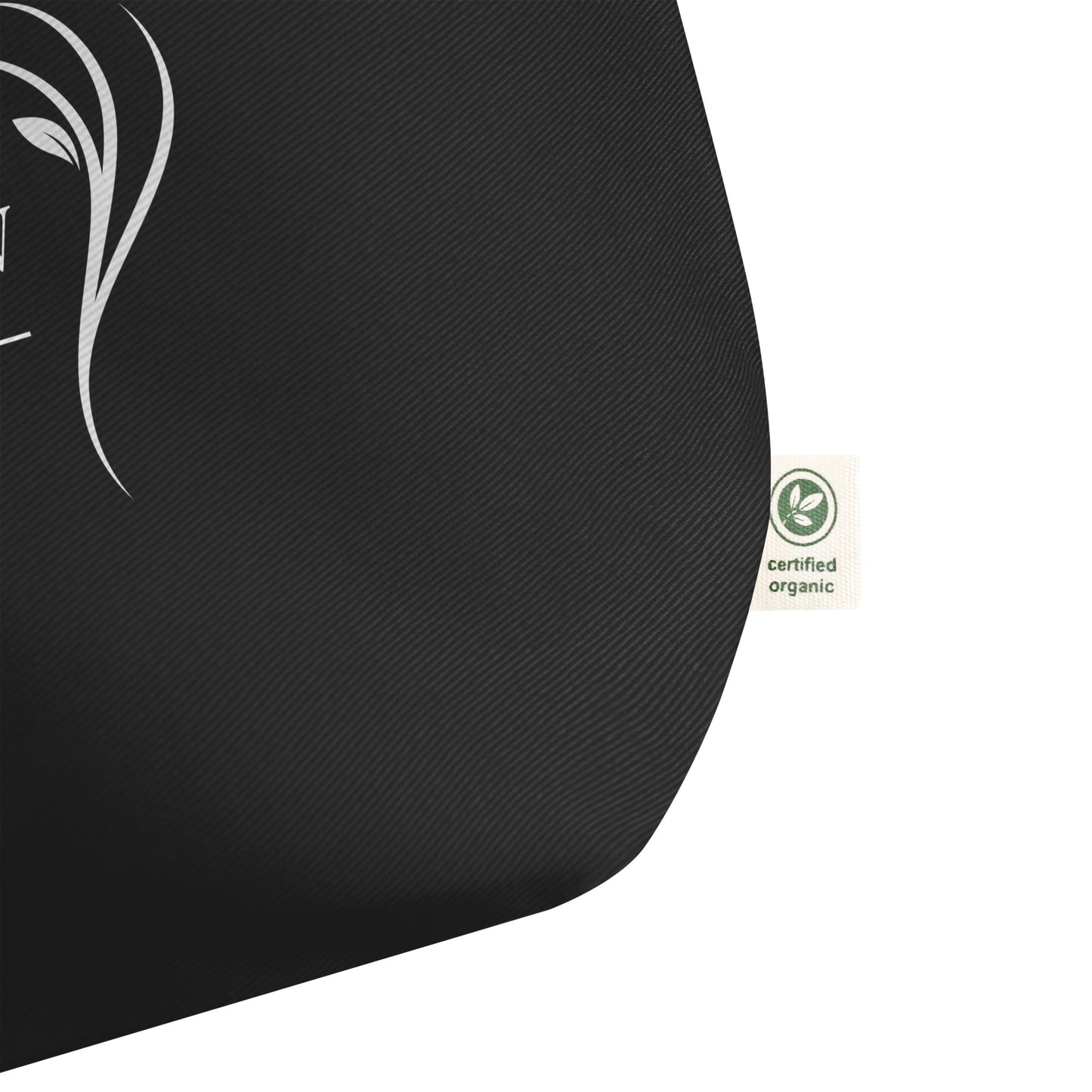 Close-up of a large black cotton Christian tote bag showing the fabric texture, certified organic side tag, and part of the white “Be Still and Know” design.
