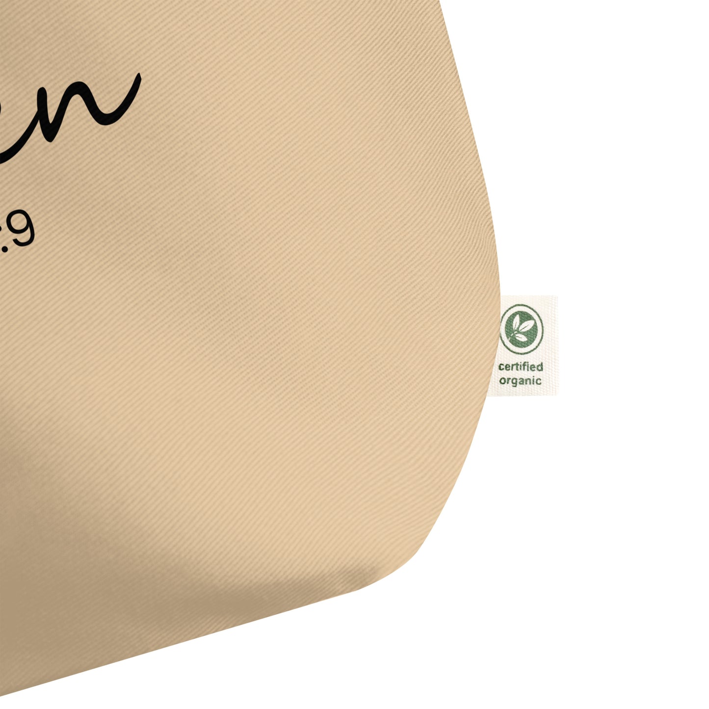 Close-up of the natural cotton tote fabric, showing the textured weave and a side “certified organic” tag detail.