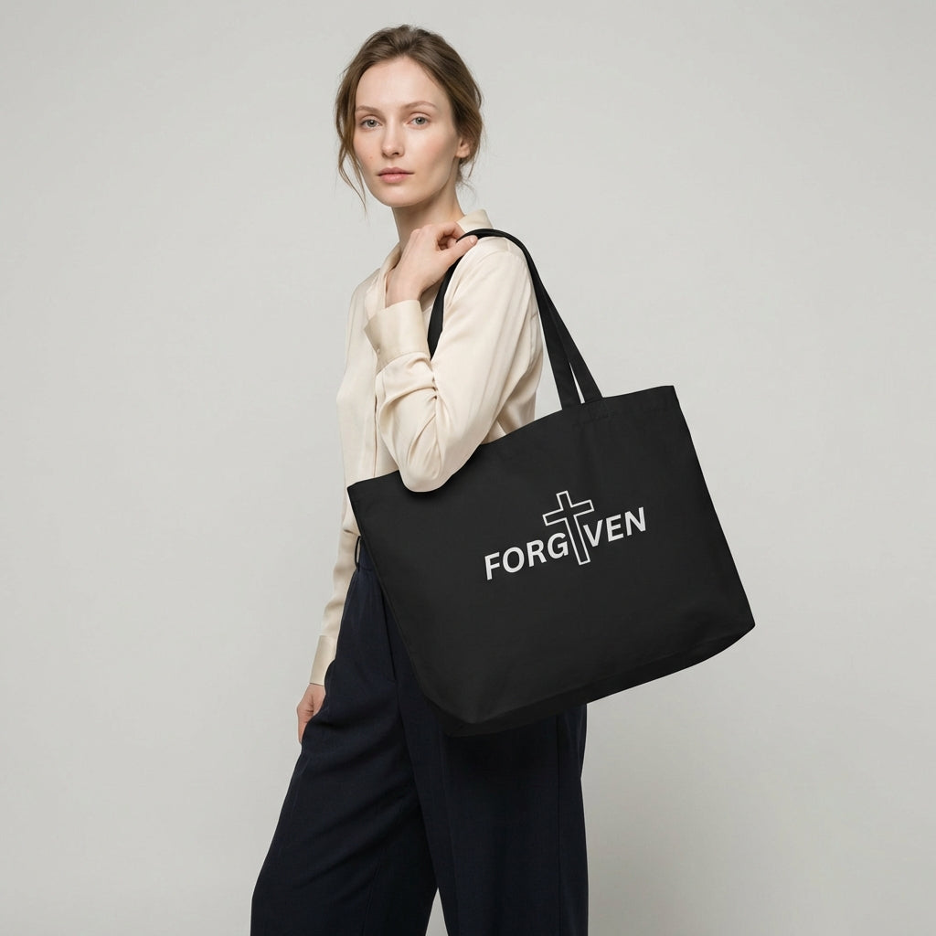 Model holding a large black cotton tote bag with “FORGIVEN” and a white cross graphic on the front.