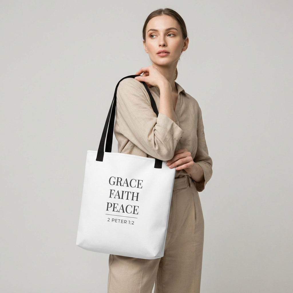 Model holding a white tote bag that reads “Grace Faith Peace” in dark gray with “2 Peter 1:2.”