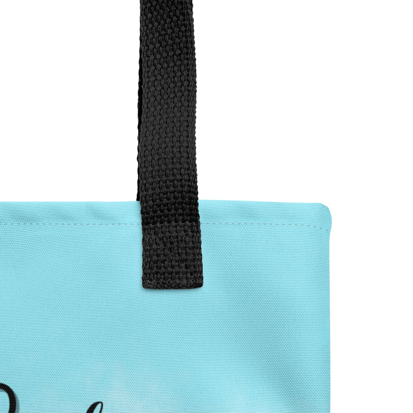 Close-up of the light blue tote fabric and black strap, highlighting the stitching, textured canvas, and strap weave detail.