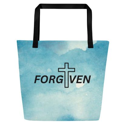 Front view of light blue watercolor tote bag with black straps and the word “FORGIVEN” with a cross replacing the letter “I.”