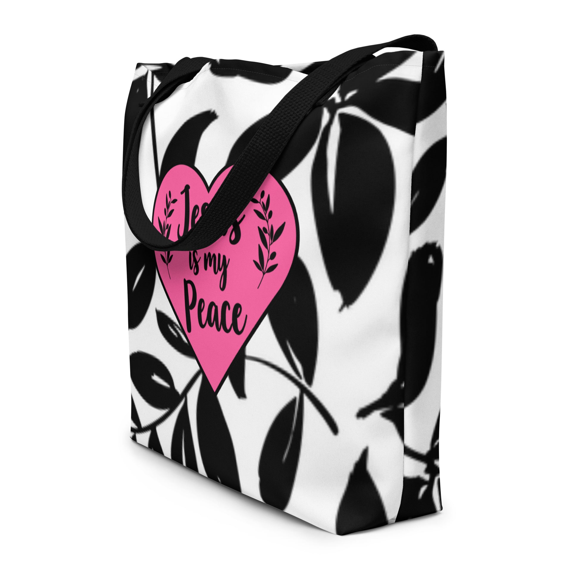 Angled view of white tote bag with black straps, black leaf print, and pink “Jesus is my Peace” heart graphic.