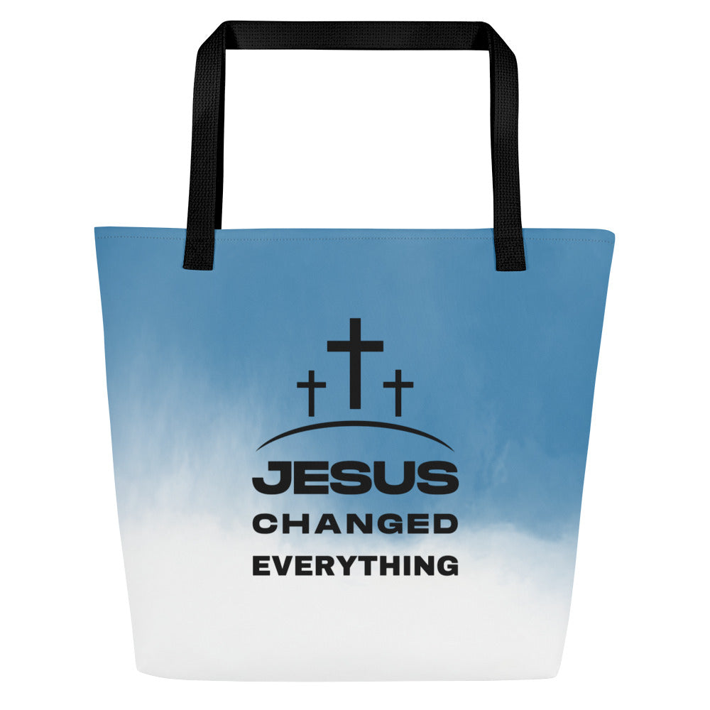 Front view of tote bag with black straps, blue-to-white ombré design, and three-cross graphic above the words “JESUS CHANGED EVERYTHING.”