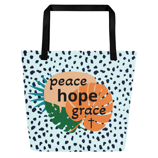 Front view of light blue tote bag with black straps, navy speckled pattern, and tropical leaf graphic with the words “peace hope grace” and a small cross.
