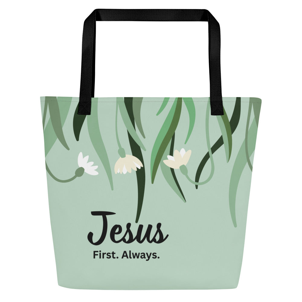 Front view of sage green tote bag with black straps, hanging greenery and small white flowers, and the text “Jesus First. Always.”