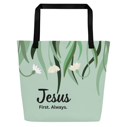 Front view of sage green tote bag with black straps, hanging greenery and small white flowers, and the text “Jesus First. Always.”