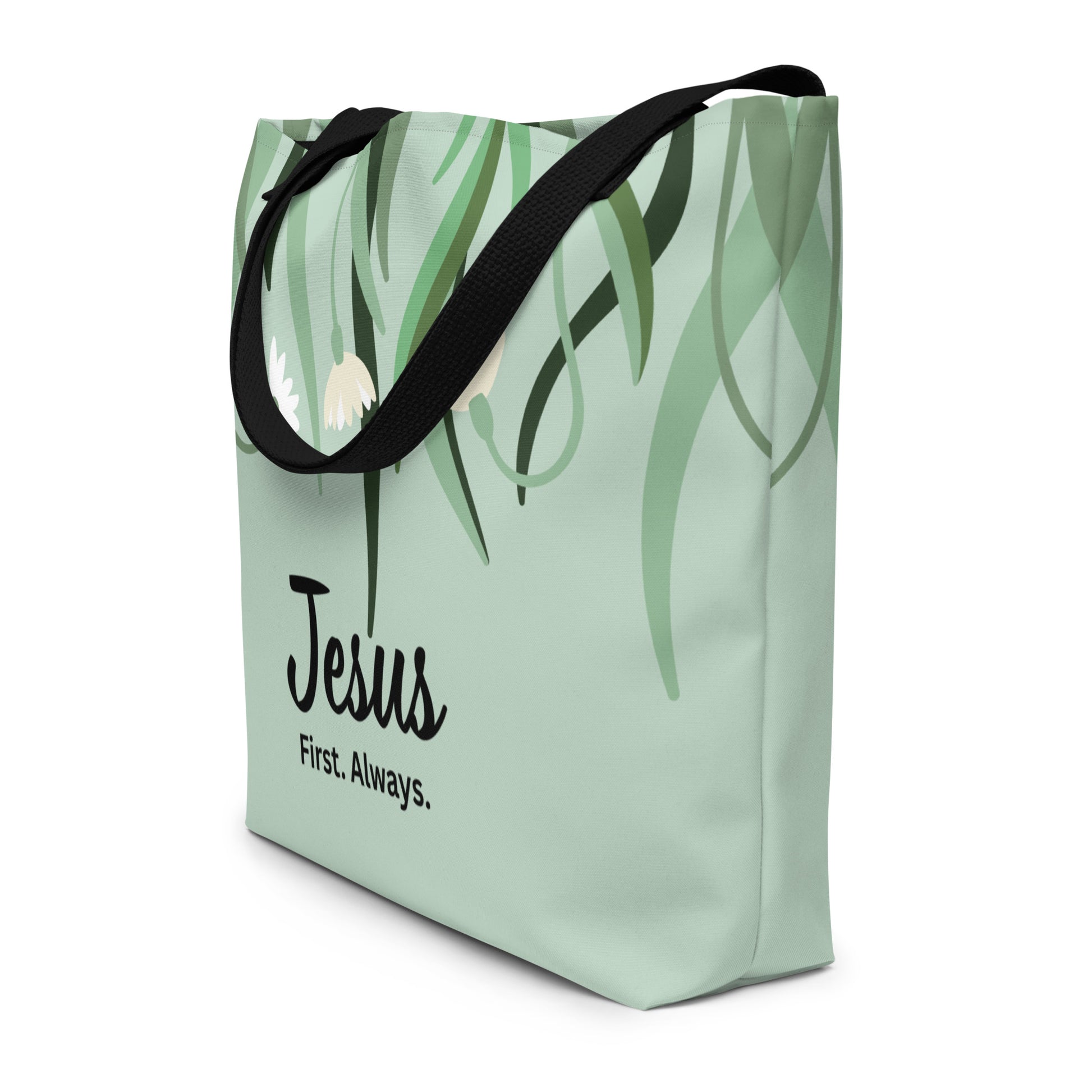 Angled view of sage green tote bag with black straps, leafy floral design, and “Jesus First. Always.” text.
