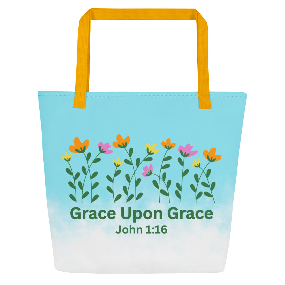 Front view of a large tote bag with yellow webbing straps. The bag fades from bright sky blue at the top into white at the bottom. Across the upper center is a row of simple wildflowers with green stems and leaves and blossoms in orange, yellow, and pink. Below the flowers, green text reads “Grace Upon Grace” with “John 1:16” underneath.
