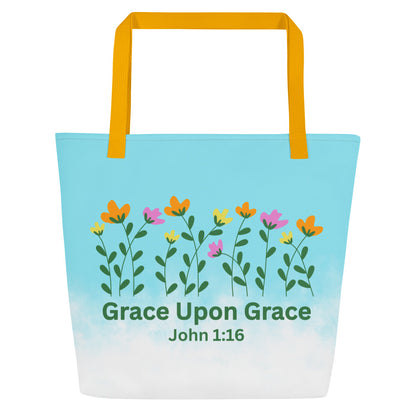 Front view of a large tote bag with yellow webbing straps. The bag fades from bright sky blue at the top into white at the bottom. Across the upper center is a row of simple wildflowers with green stems and leaves and blossoms in orange, yellow, and pink. Below the flowers, green text reads “Grace Upon Grace” with “John 1:16” underneath.