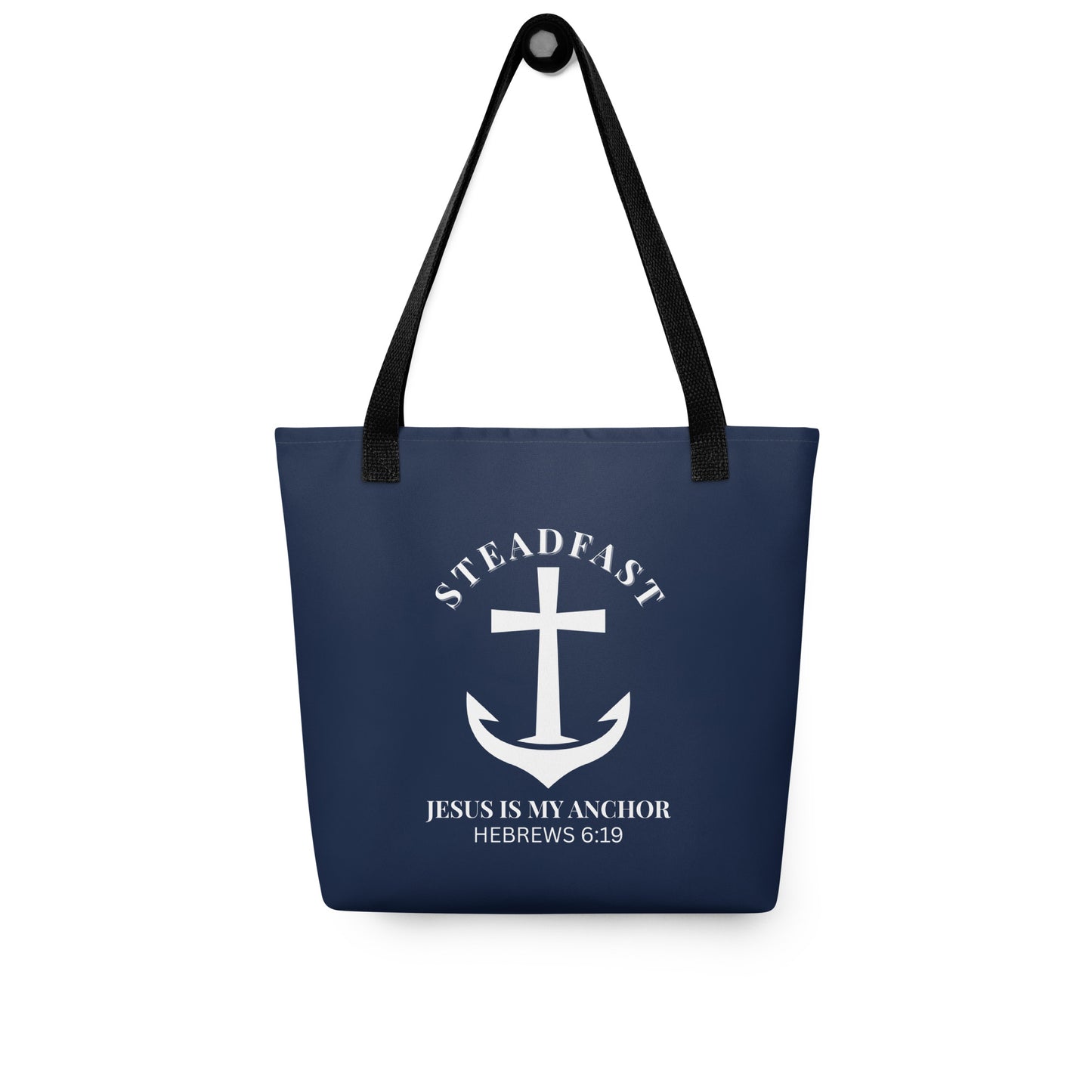 Navy blue tote bag with black straps hanging on a hook, displaying a white anchor-and-cross emblem with “STEADFAST” and “JESUS IS MY ANCHOR” (Hebrews 6:19).