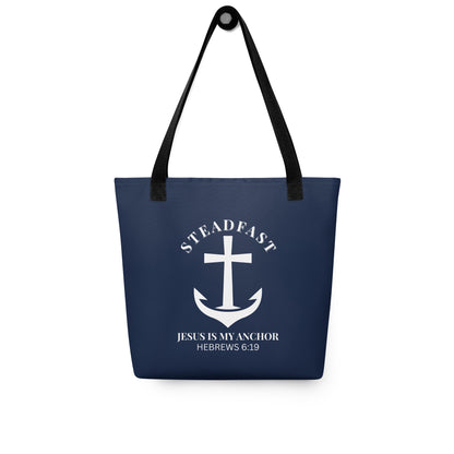 Navy blue tote bag with black straps hanging on a hook, displaying a white anchor-and-cross emblem with “STEADFAST” and “JESUS IS MY ANCHOR” (Hebrews 6:19).