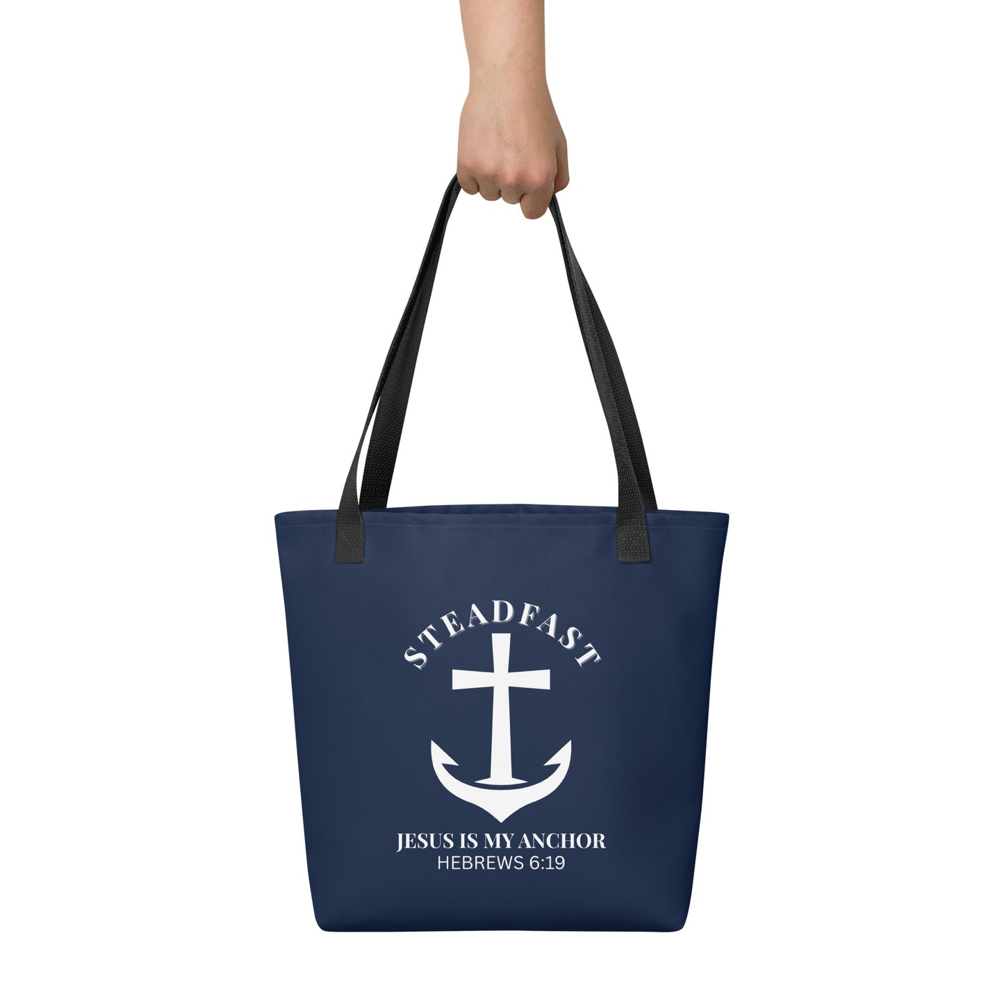 Tote bag held by hand with black straps, featuring a navy background and a white anchor cross graphic with the words “STEADFAST” and “JESUS IS MY ANCHOR” and the verse “HEBREWS 6:19.”