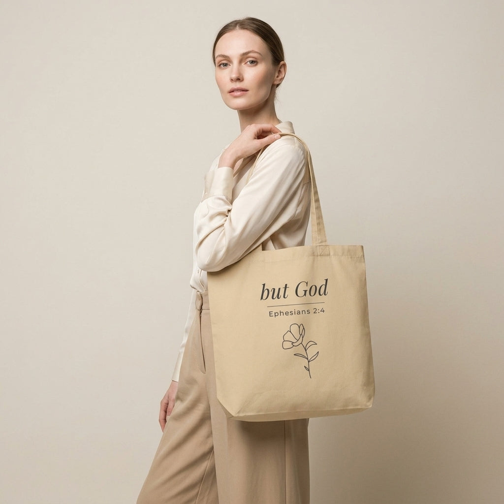 Model carrying a natural cotton Christian tote bag with beige handles and a minimalist “but God Ephesians 2:4” design.
