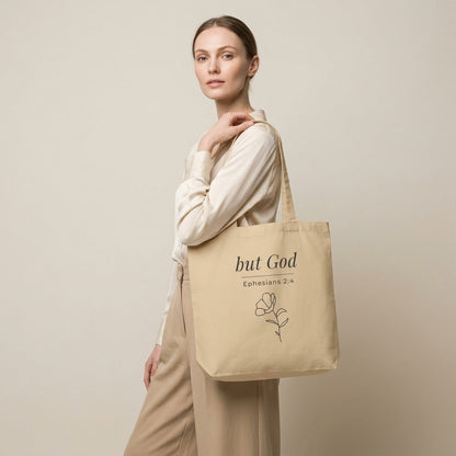 Model carrying a natural cotton Christian tote bag with beige handles and a minimalist “but God Ephesians 2:4” design.