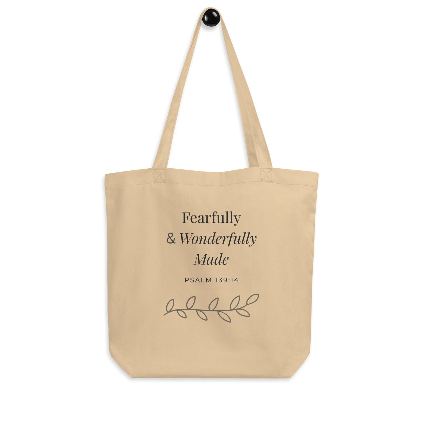 Natural cotton Christian tote bag hanging on a hook, featuring beige straps, gray lettering, and a minimalist Psalm 139:14 faith design.