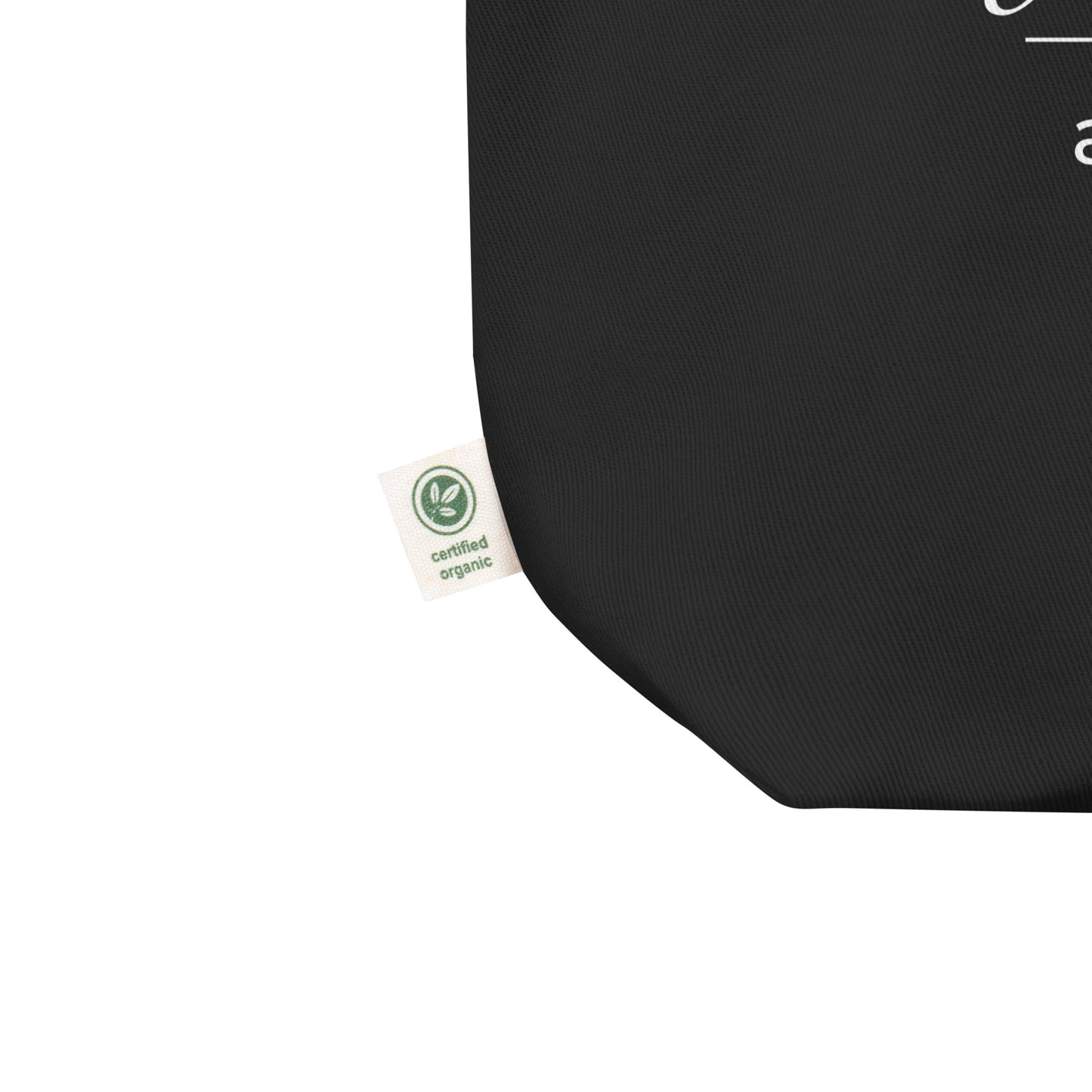 Close-up of a black cotton Christian tote bag showing the fabric texture, certified organic side tag, and part of the white “God is good all the time” design.