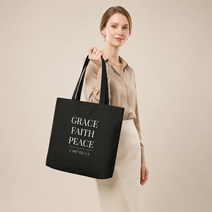 Model carrying a black cotton Christian tote bag with matching black handles and a minimalist “Grace Faith Peace” 2 Peter 1:2 design.