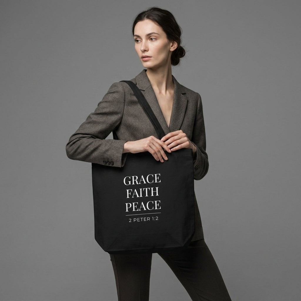 Model carrying a black cotton Christian tote bag with matching black handles and a minimalist “Grace Faith Peace” 2 Peter 1:2 design.