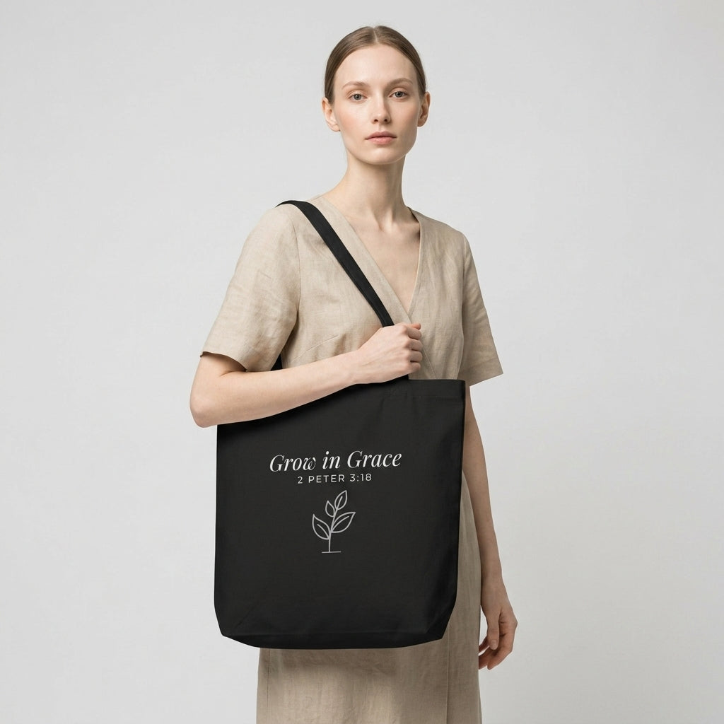 Model carrying a black cotton Christian tote bag with matching black handles, a “Grow in Grace” scripture design, and a small sprouting plant illustration.