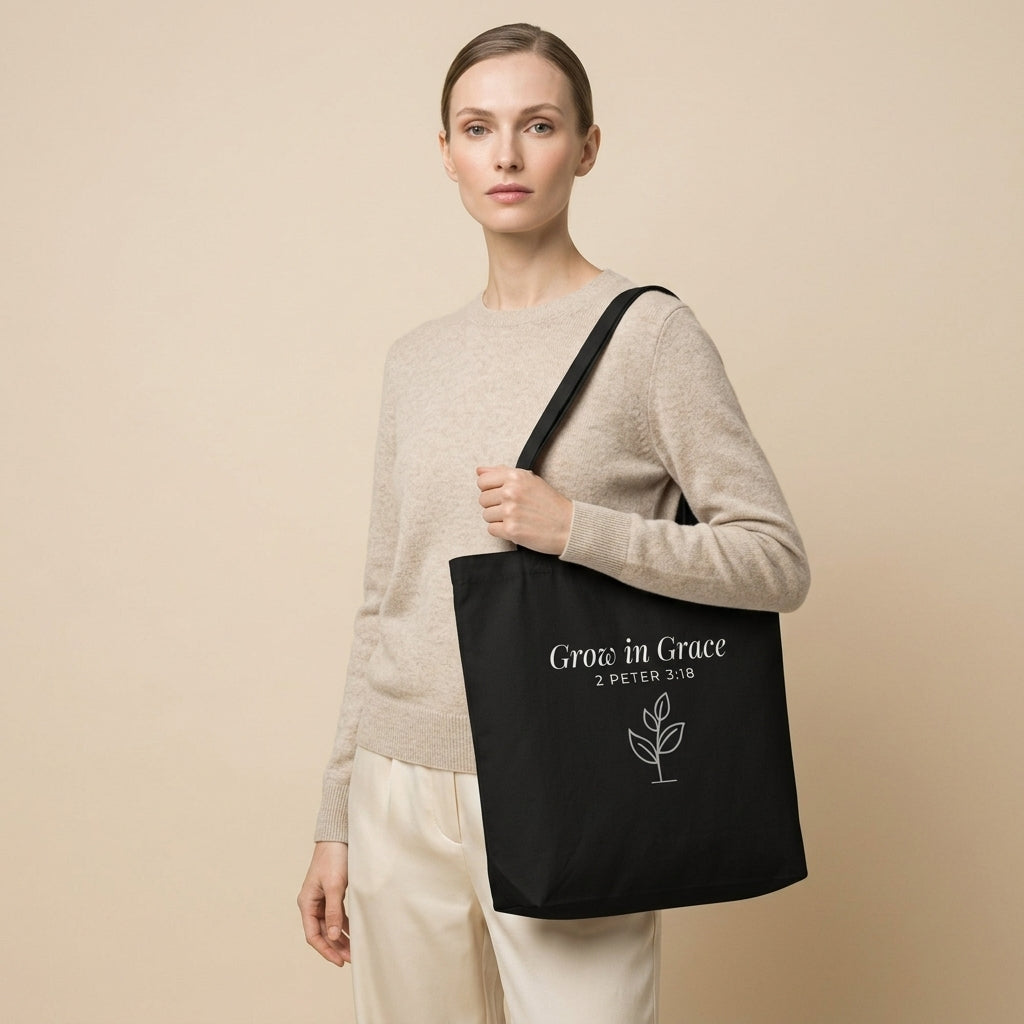 Model carrying a black cotton Christian tote bag with matching black handles, a “Grow in Grace” scripture design, and a small sprouting plant illustration.