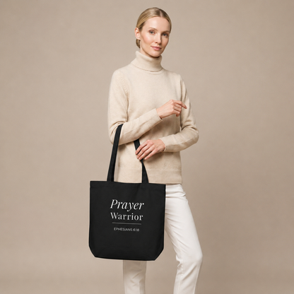 Model carrying a black cotton Christian tote bag with matching black handles and a white “Prayer Warrior Ephesians 6:18” design.