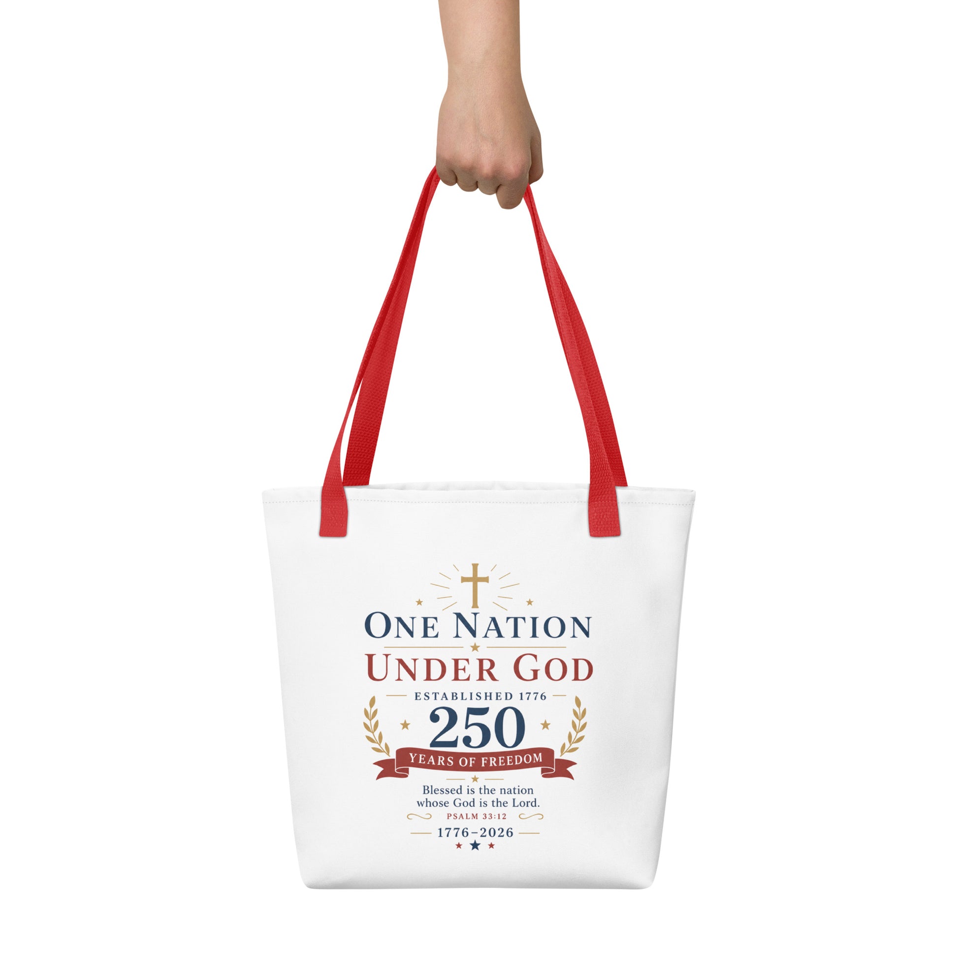 Person holding a white Christian tote bag with red handles, patriotic artwork, and “One Nation Under God 250 Years of Freedom” text.