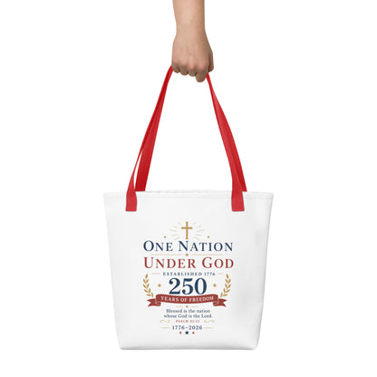 Person holding a white Christian tote bag with red handles, patriotic artwork, and “One Nation Under God 250 Years of Freedom” text.
