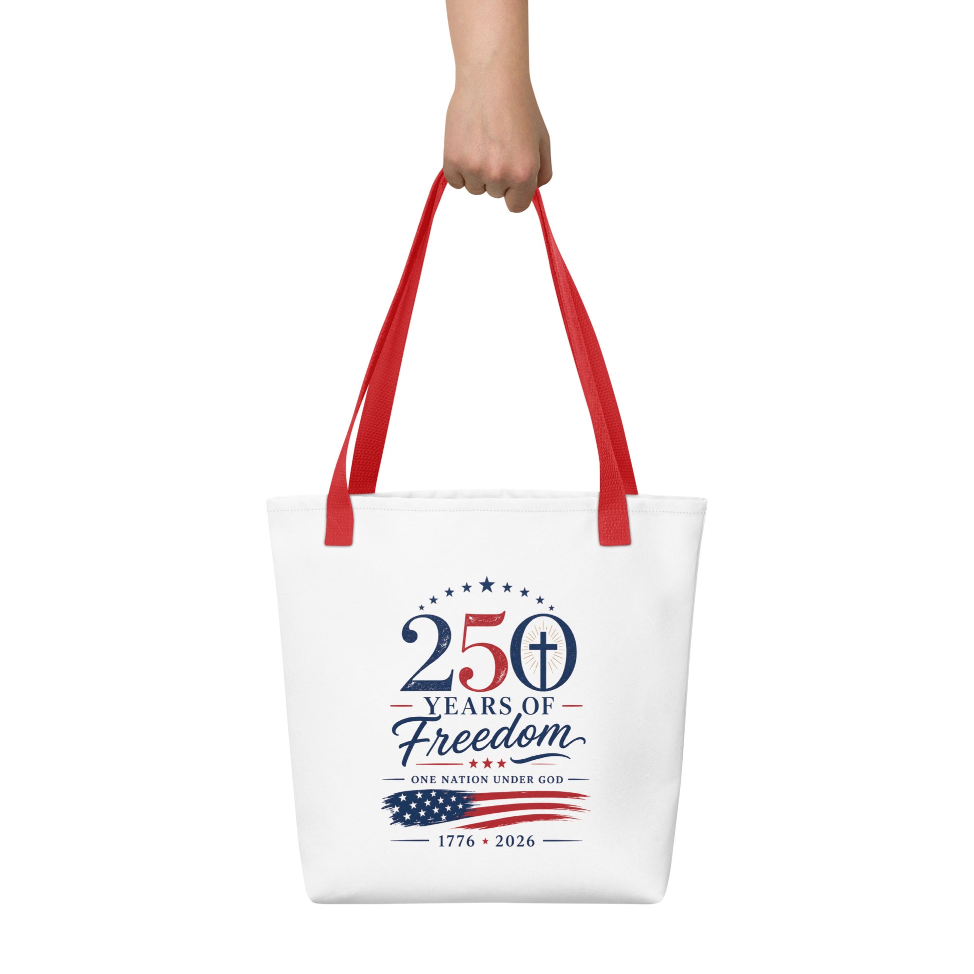 Person holding a white Christian tote bag with red handles, patriotic lettering, an American flag graphic, and “One Nation Under God” text.