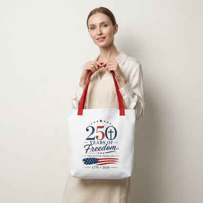 Model carrying a white Christian Fourth of July tote bag with red handles and a “250 Years of Freedom, One Nation Under God” design.