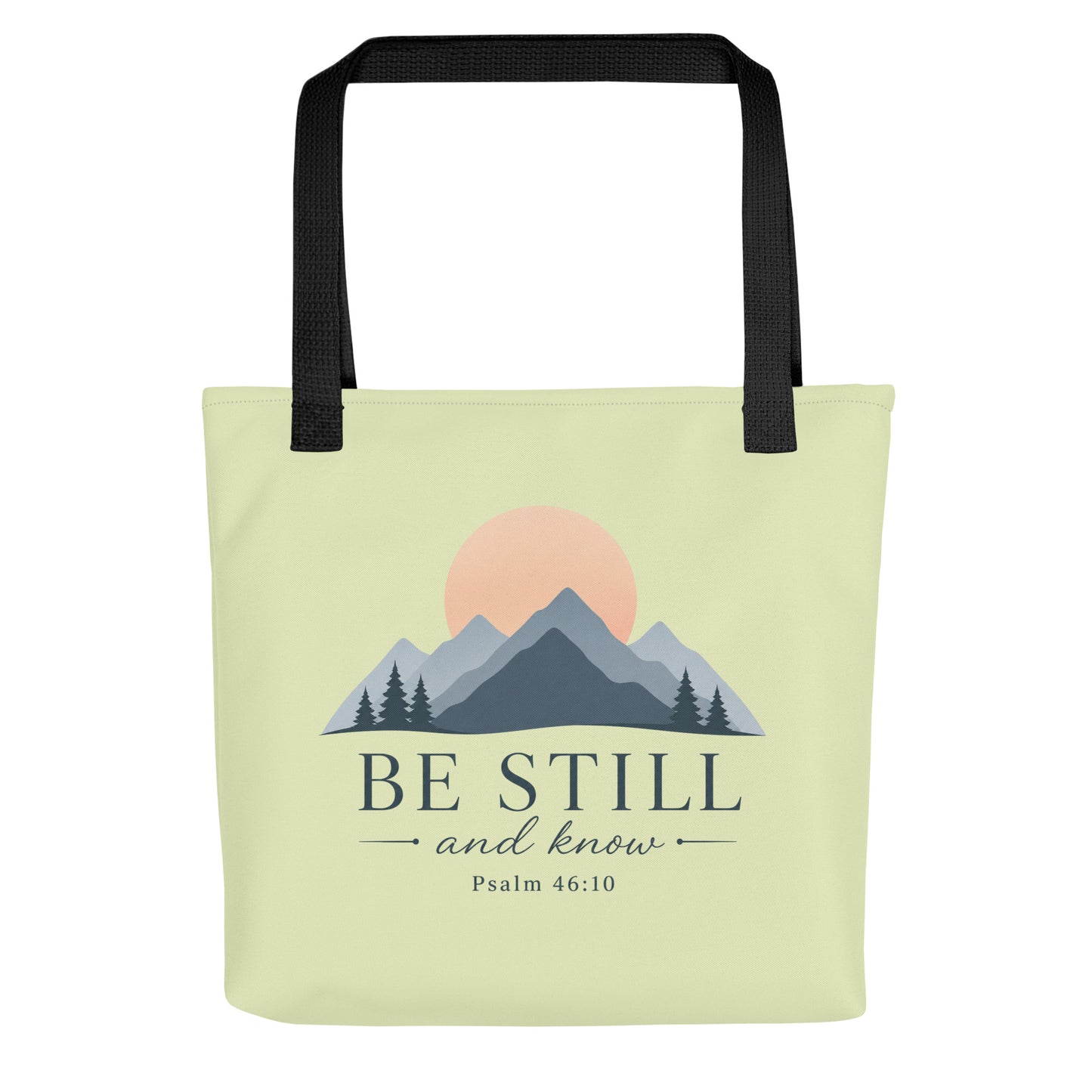 Front view of a light green Christian tote bag with black handles, mountain artwork, a sunrise, and the text “Be Still and Know Psalm 46:10.”