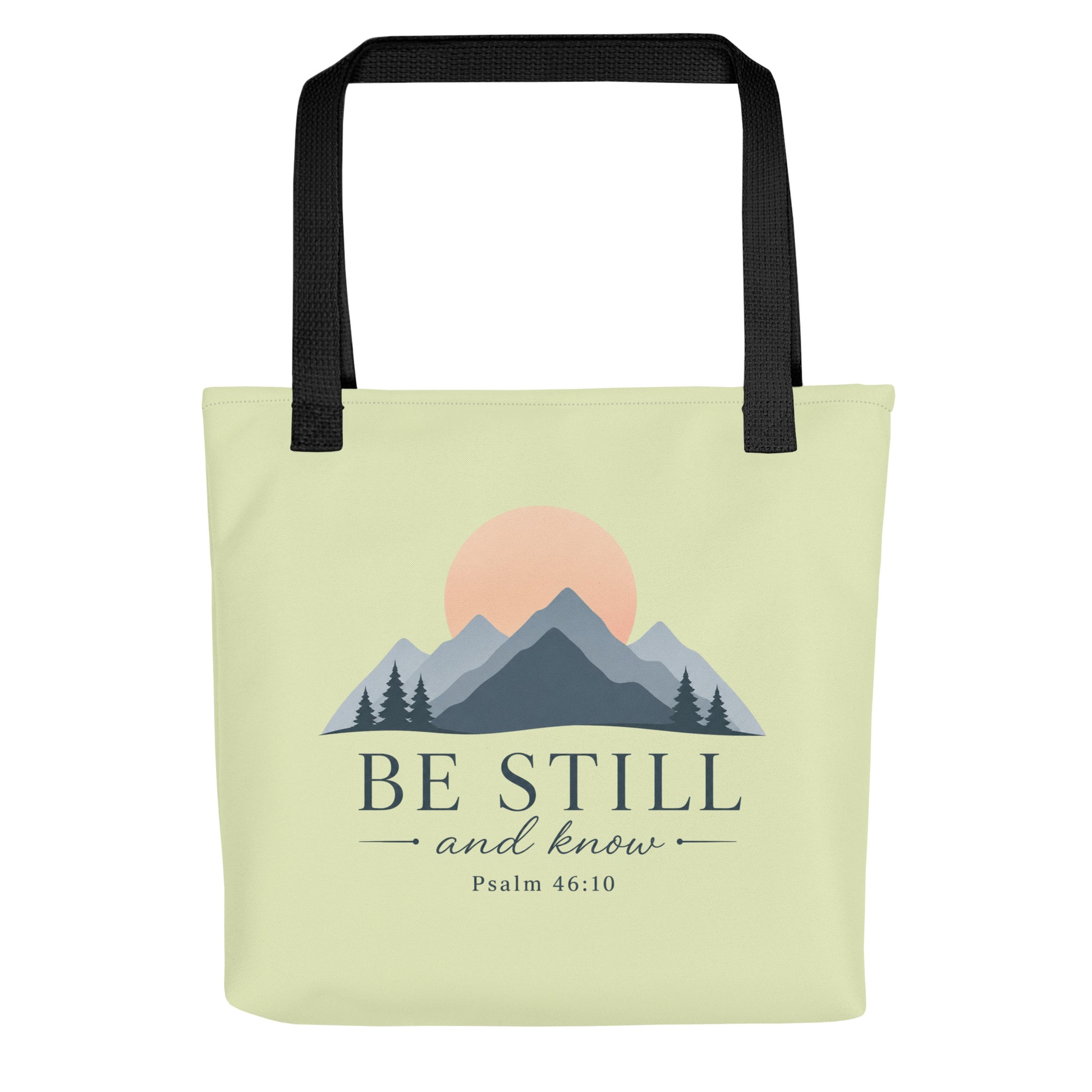 Front view of a light green Christian tote bag with black handles, mountain artwork, a sunrise, and the text “Be Still and Know Psalm 46:10.”