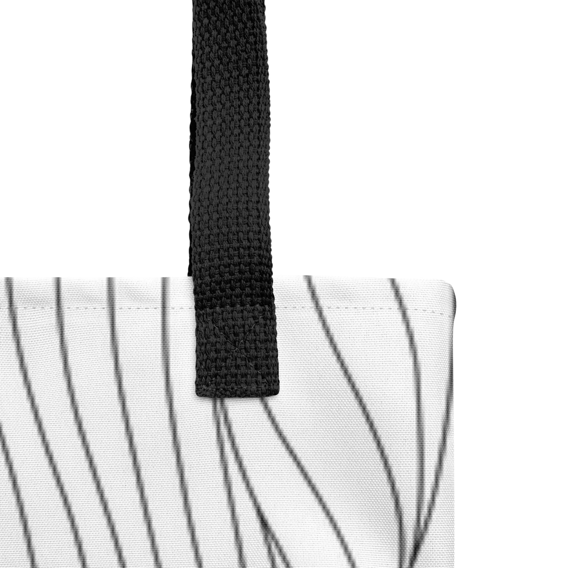 Close-up of the white tote fabric and black strap, highlighting the stitching, textured canvas, and black curved line pattern.