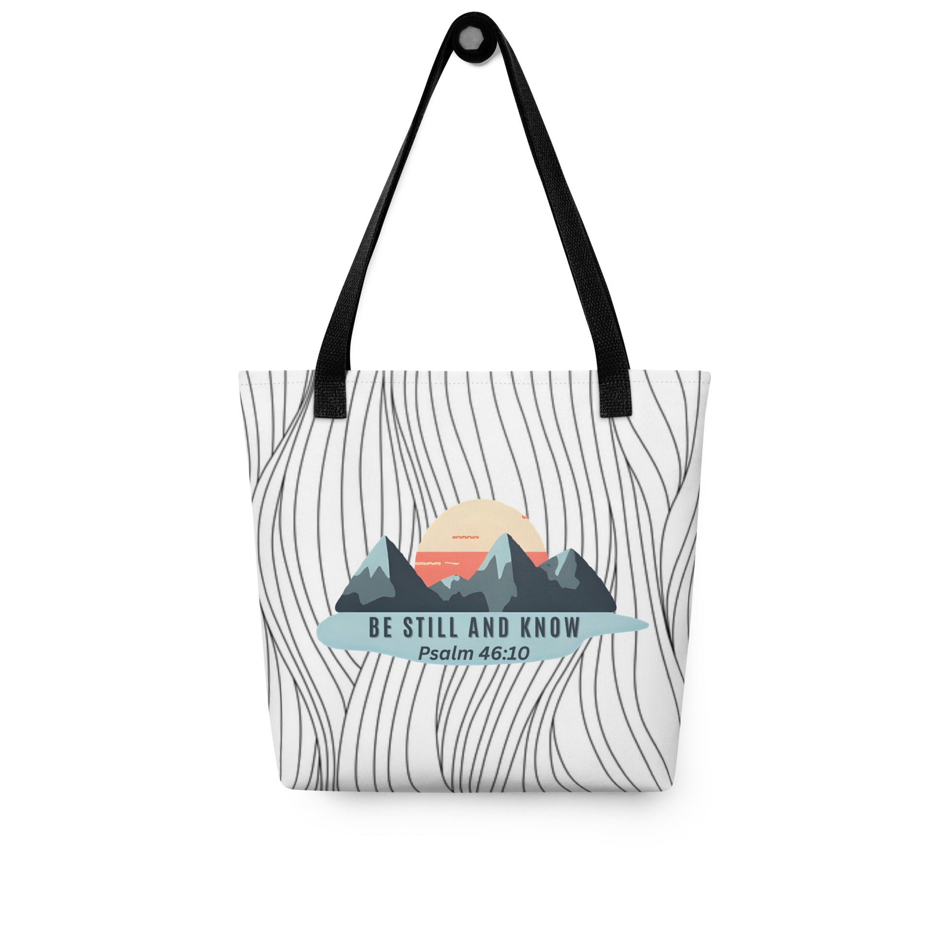 Tote bag hanging on a hook with black handles, wavy line background, and “BE STILL AND KNOW — Psalm 46:10” mountain graphic.
