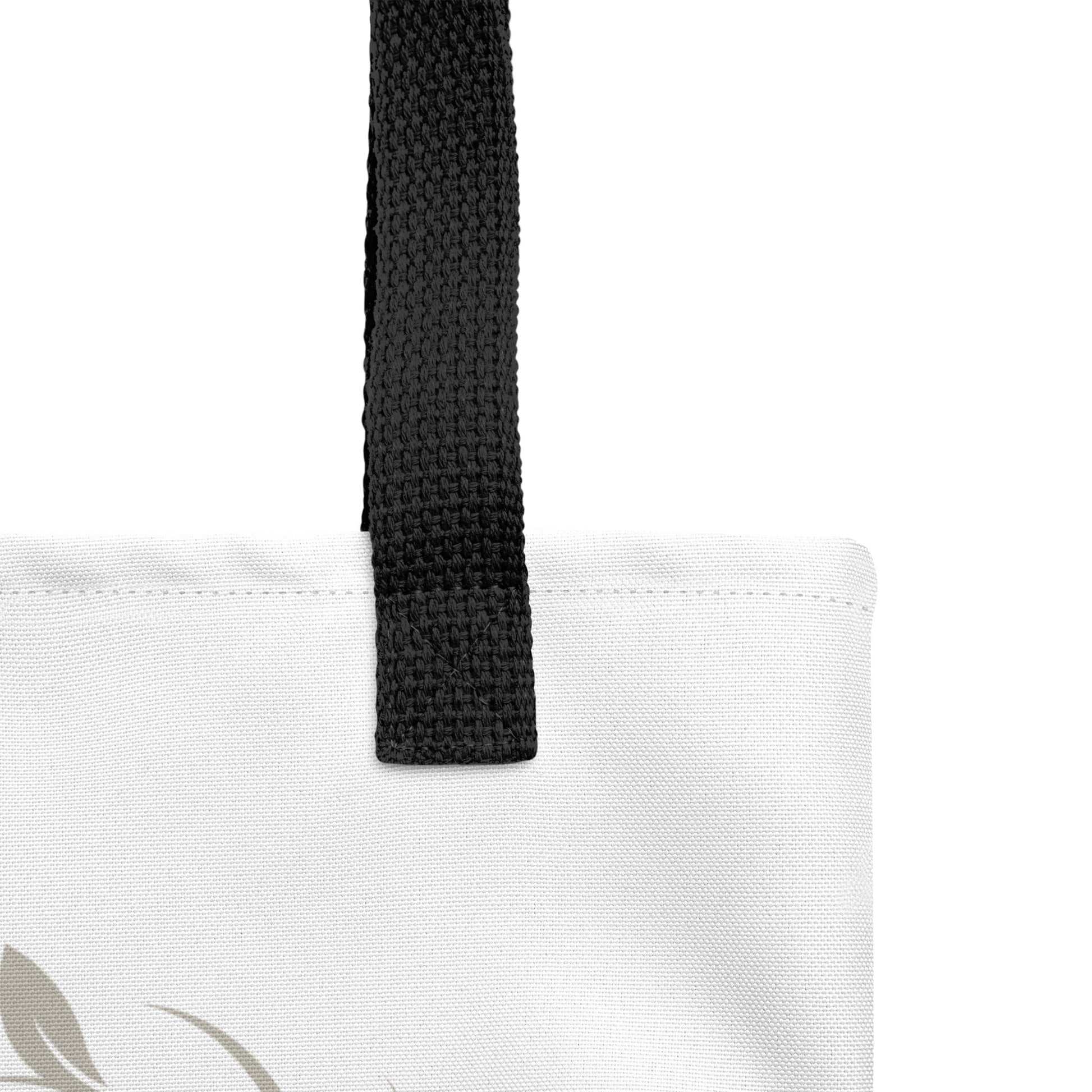 Close-up of the white tote fabric and black strap, highlighting the stitching, textured canvas, and strap weave detail.