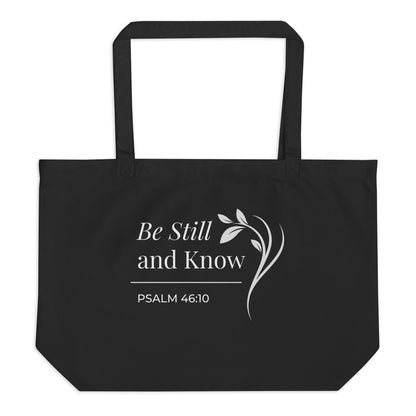 Front view of a large black cotton Christian tote bag with matching black handles and a white “Be Still and Know Psalm 46:10” design.