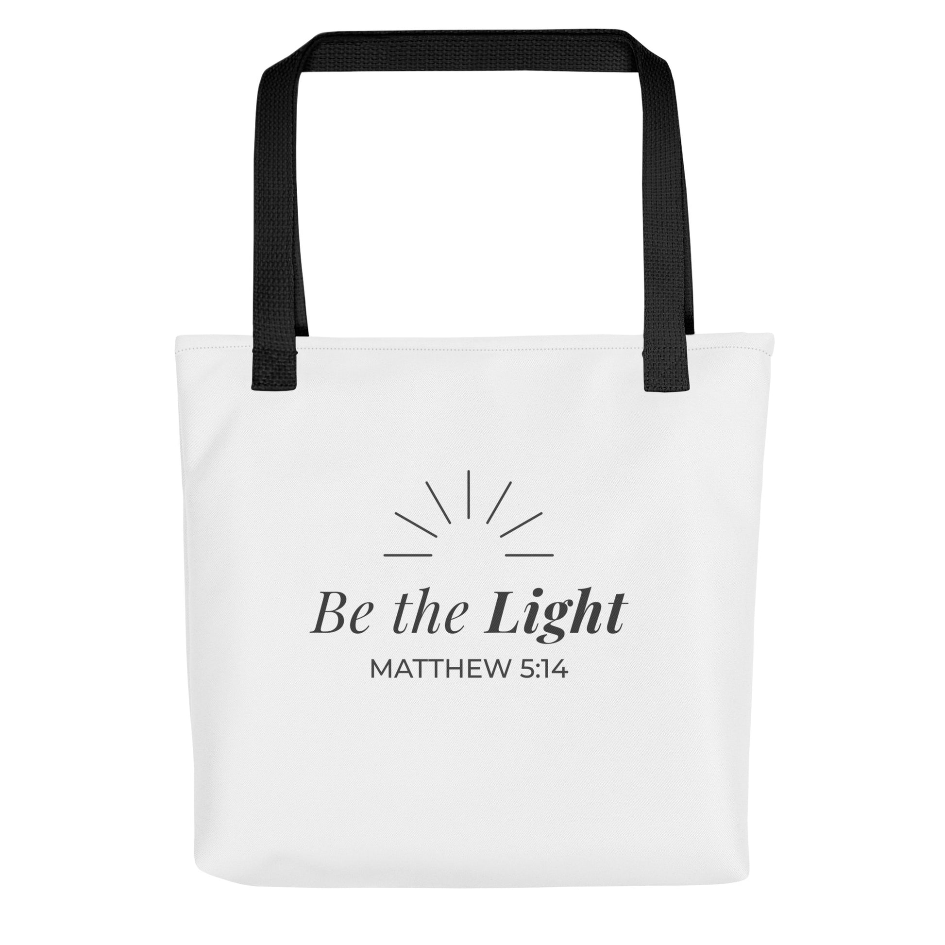 Front view of a white tote bag with black handles featuring “Be the Light,” “Matthew 5:14,” and a sunburst design in dark gray.