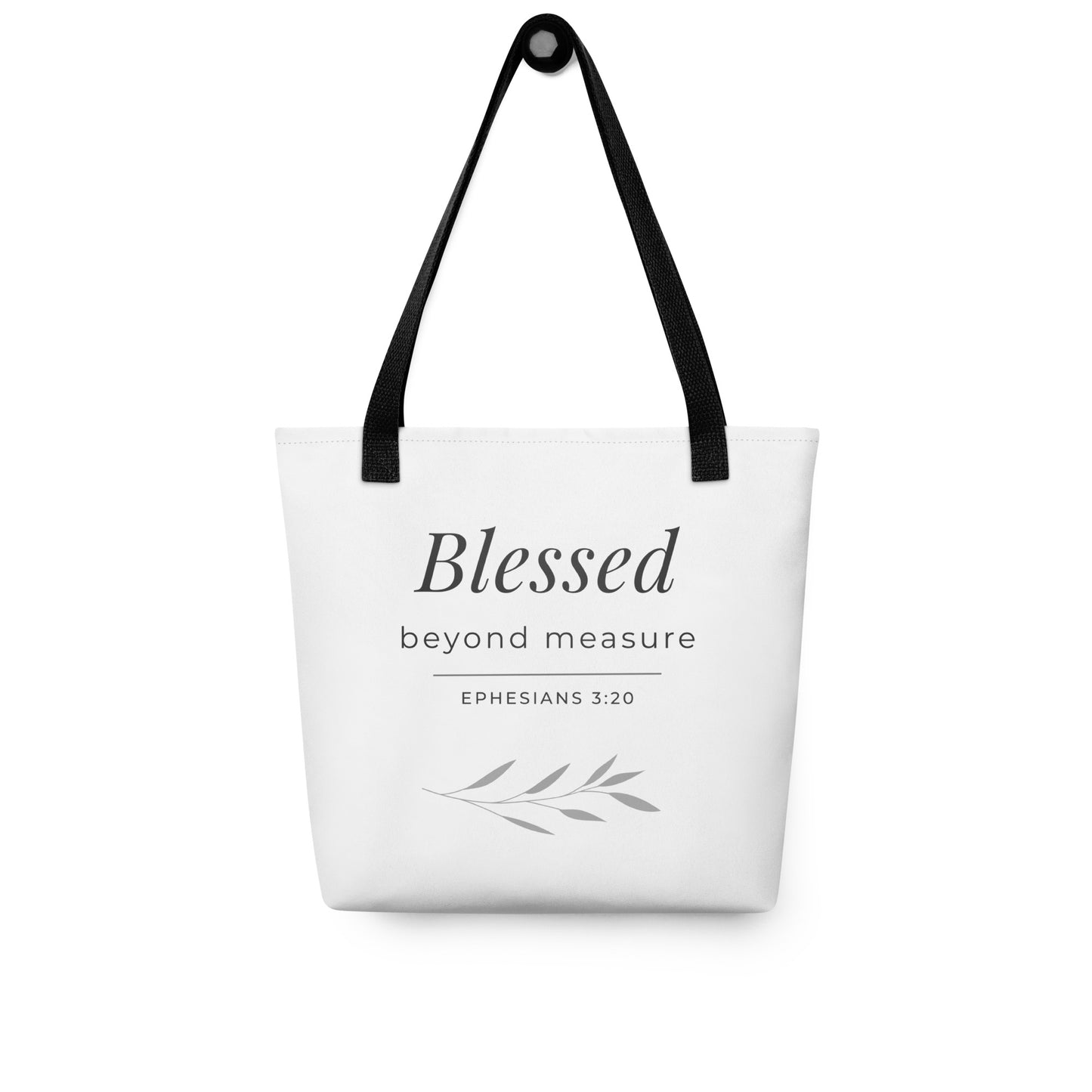 White tote bag hanging on a hook with black handles featuring “Blessed beyond measure” and “Ephesians 3:20” in dark gray with a leaf design.