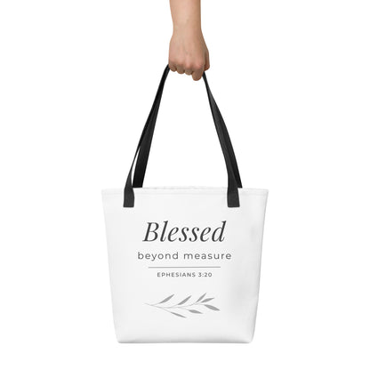 White tote bag held in hand with black handles featuring “Blessed beyond measure” and “Ephesians 3:20” in dark gray with a leaf design.