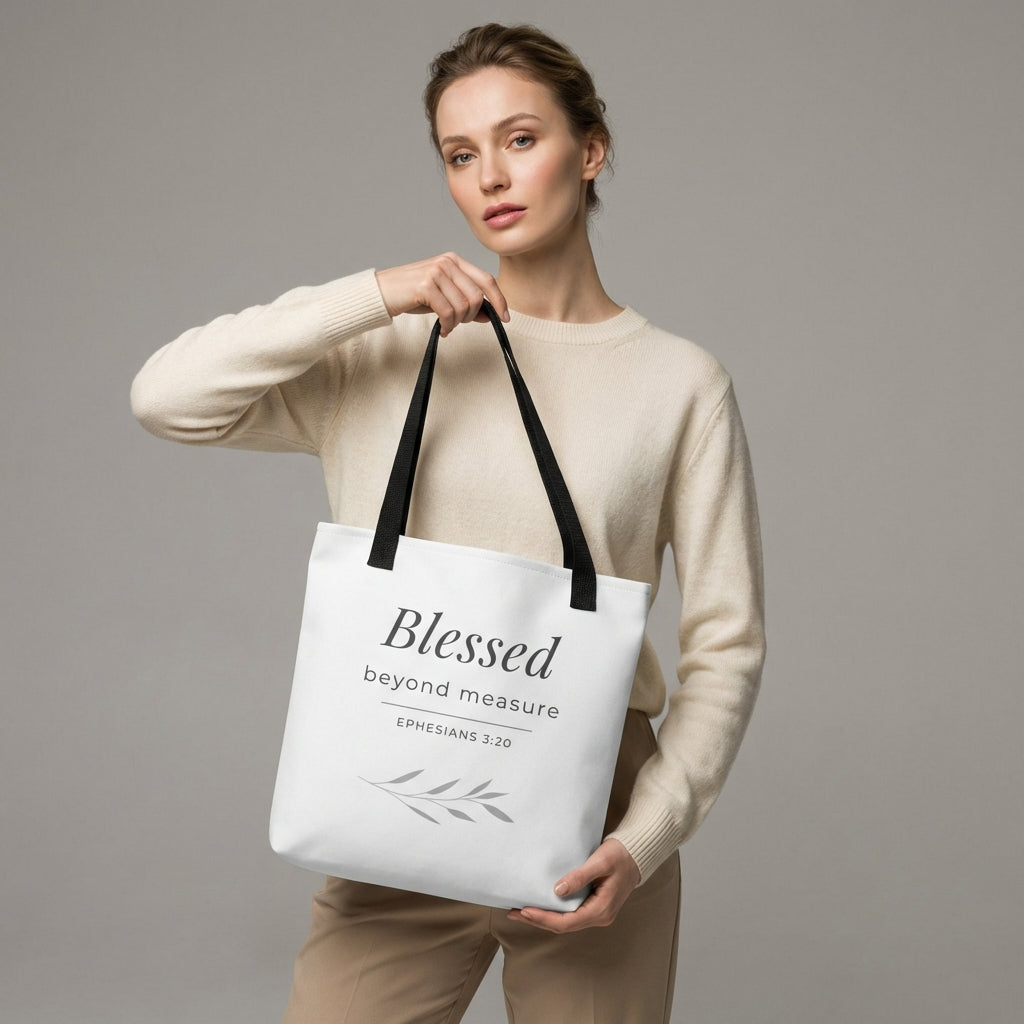 Lifestyle photo of a model holding a white tote bag with black handles featuring “Blessed beyond measure” and “Ephesians 3:20” with a leaf design.