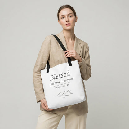 Lifestyle photo of a model holding a white tote bag with black handles featuring “Blessed beyond measure” and “Ephesians 3:20” with a leaf design.
