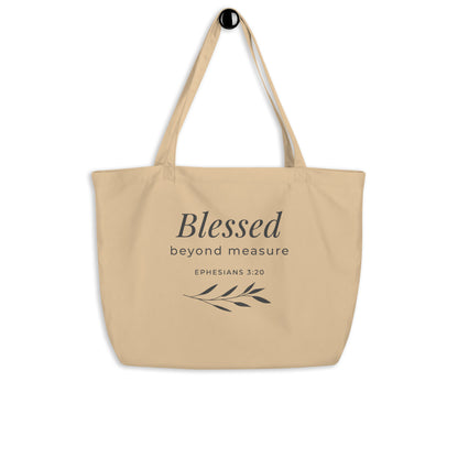 Natural cotton Christian tote bag hanging on a hook, featuring beige straps, gray lettering, and a simple “Blessed Beyond Measure” faith design.