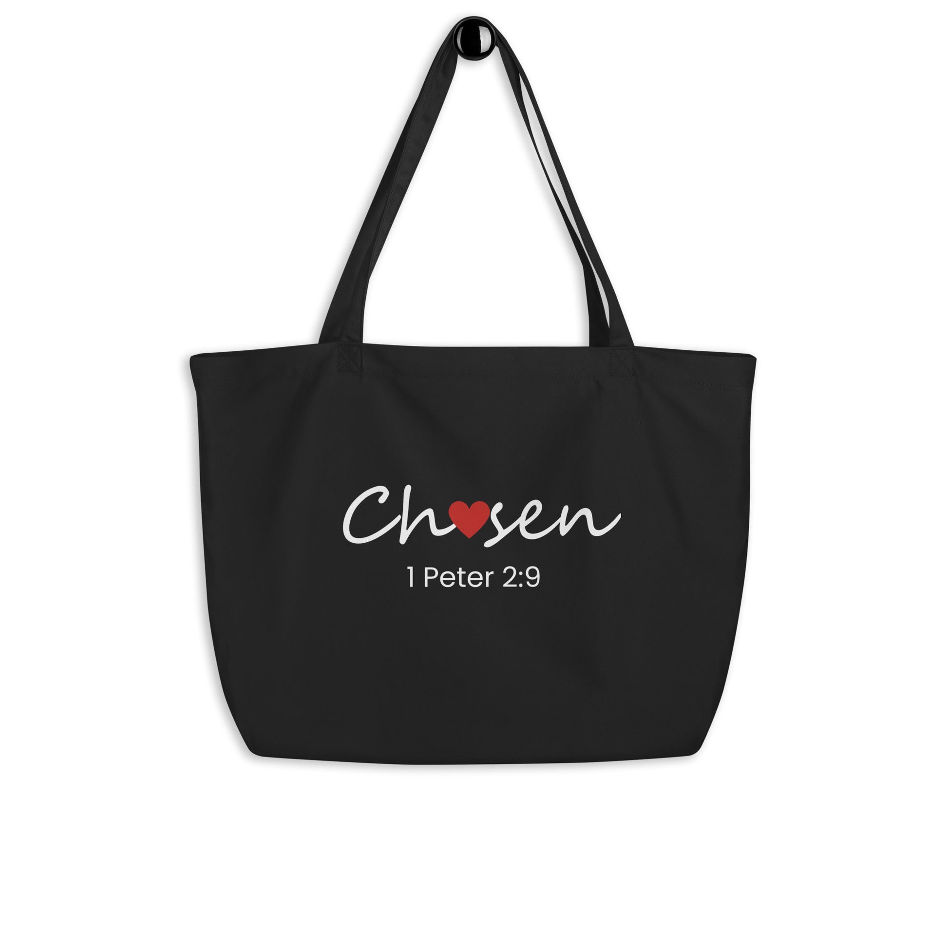 Black tote bag hanging on a hook featuring “Chosen” with a red heart and “1 Peter 2:9” in white text.