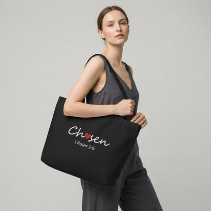 Lifestyle photo of a model holding a black tote bag featuring “Chosen” with a red heart and “1 Peter 2:9.”
