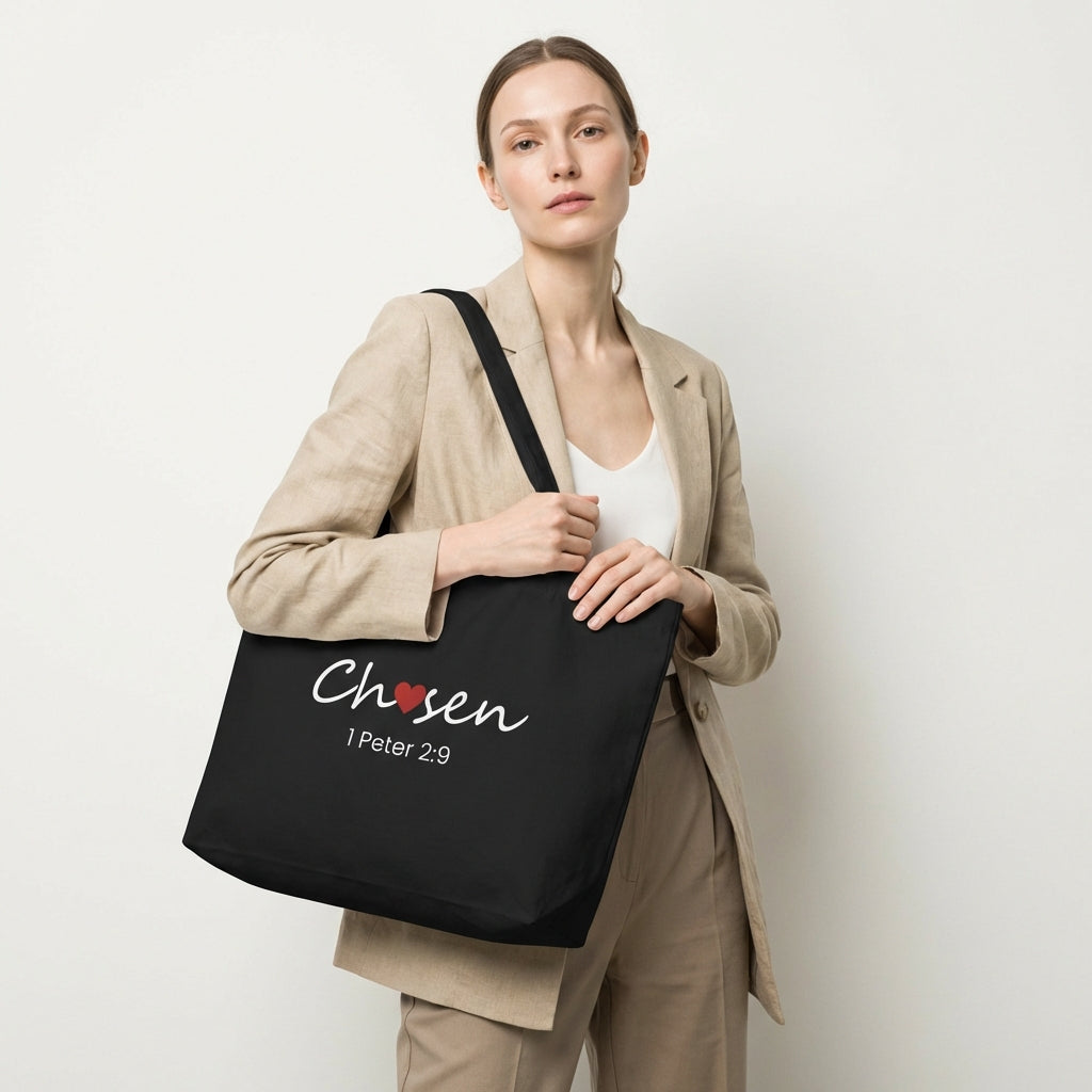 Lifestyle photo of a model holding a black tote bag featuring “Chosen” with a red heart and “1 Peter 2:9.”