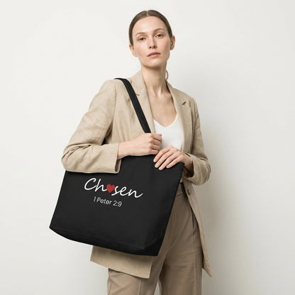 Lifestyle photo of a model holding a black tote bag featuring “Chosen” with a red heart and “1 Peter 2:9.”