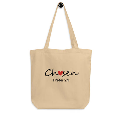 Natural cotton tote bag hanging on a hook featuring “Chosen” with a red heart detail and “1 Peter 2:9” below.