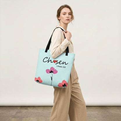 Woman modeling a light blue Christian tote bag with black straps, floral artwork, and the word “Chosen” with the Bible verse “1 Peter 2:9” printed on the front.