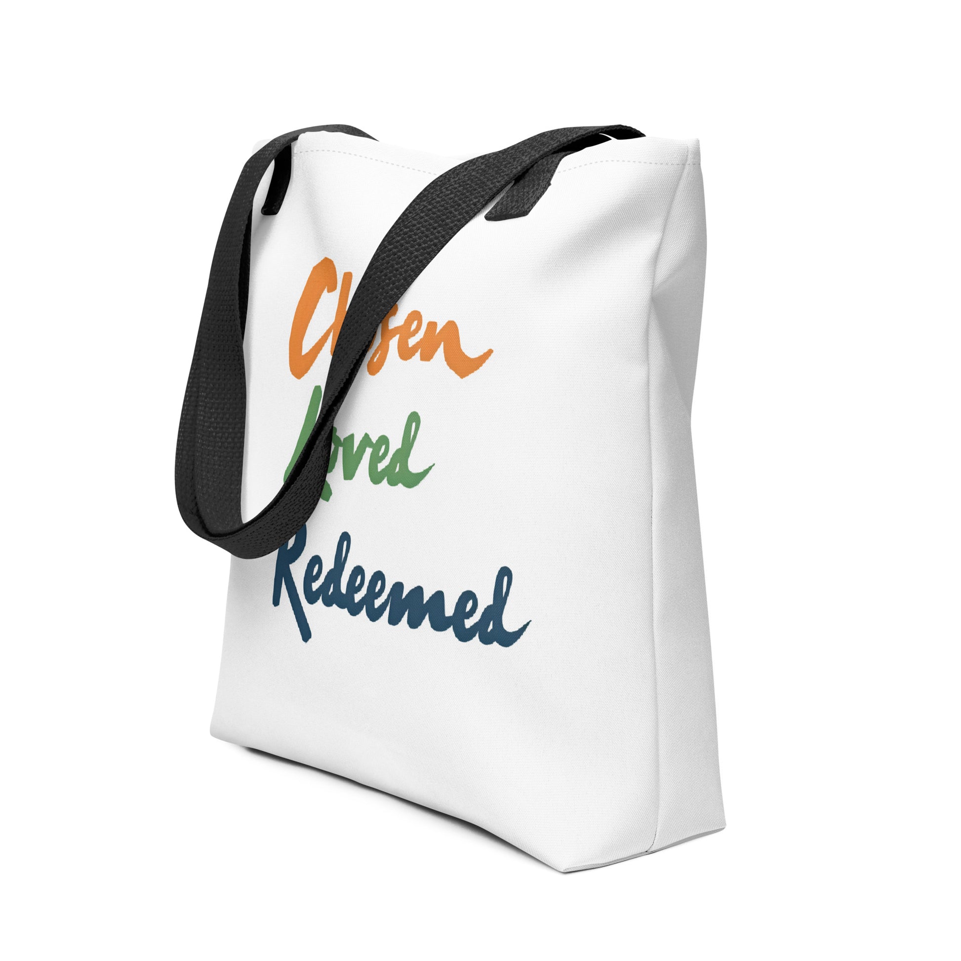 Angled view of a white tote with black straps showing “Chosen Loved Redeemed” in colorful script lettering.