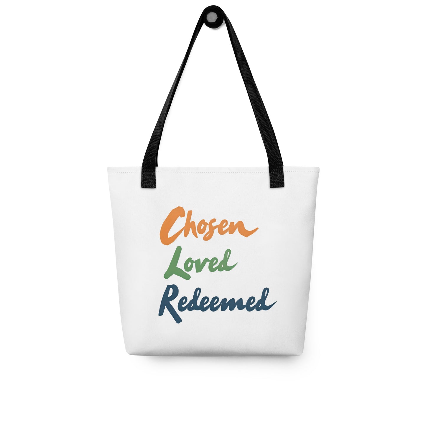 White tote bag hanging on a hook with black handles and “Chosen Loved Redeemed” in orange, green, and navy text.